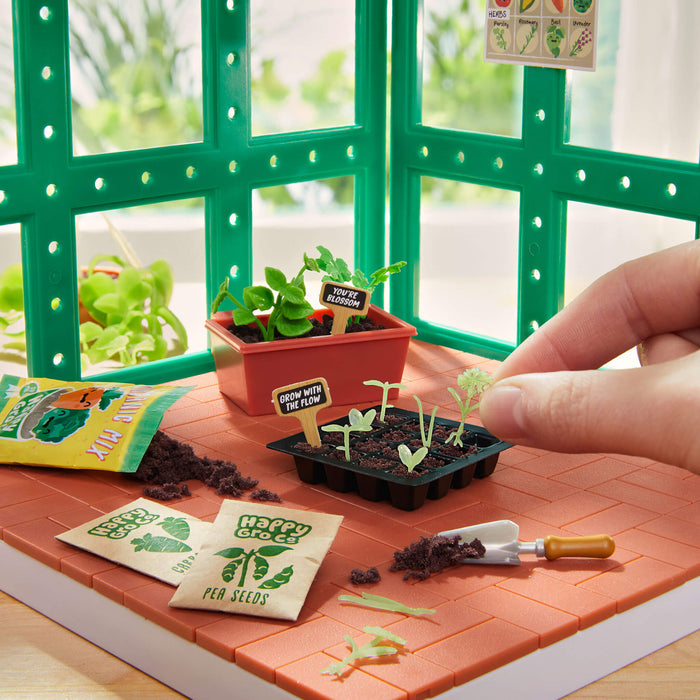 Miniature gardening setup with seed packets, soil, and small plants on a tiled surface.