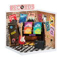 Miniature record store display with vinyl records, guitar, and amplifier against a brick wall.